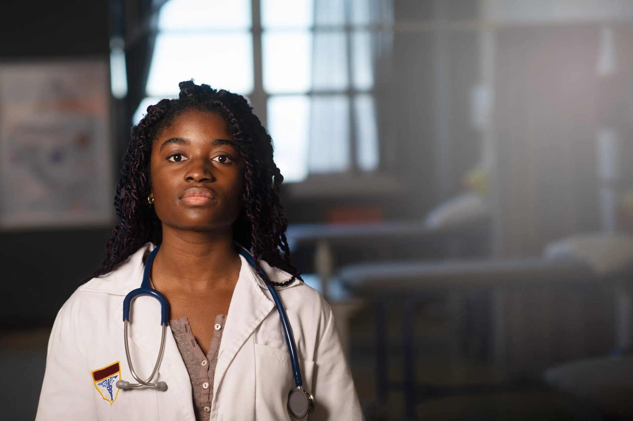A doctor in a white coat with a stethoscope, standing in a hospital ward