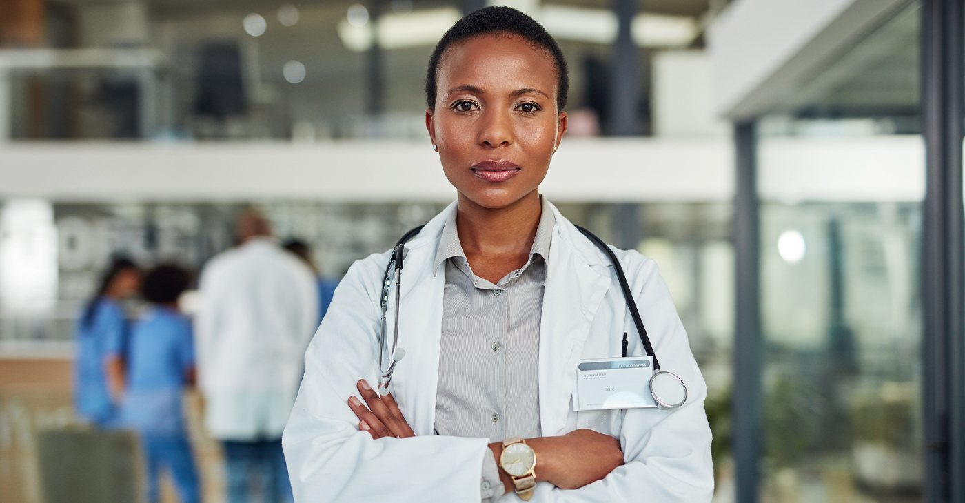 A doctor in a white coat standing with arms folded in a hospital
