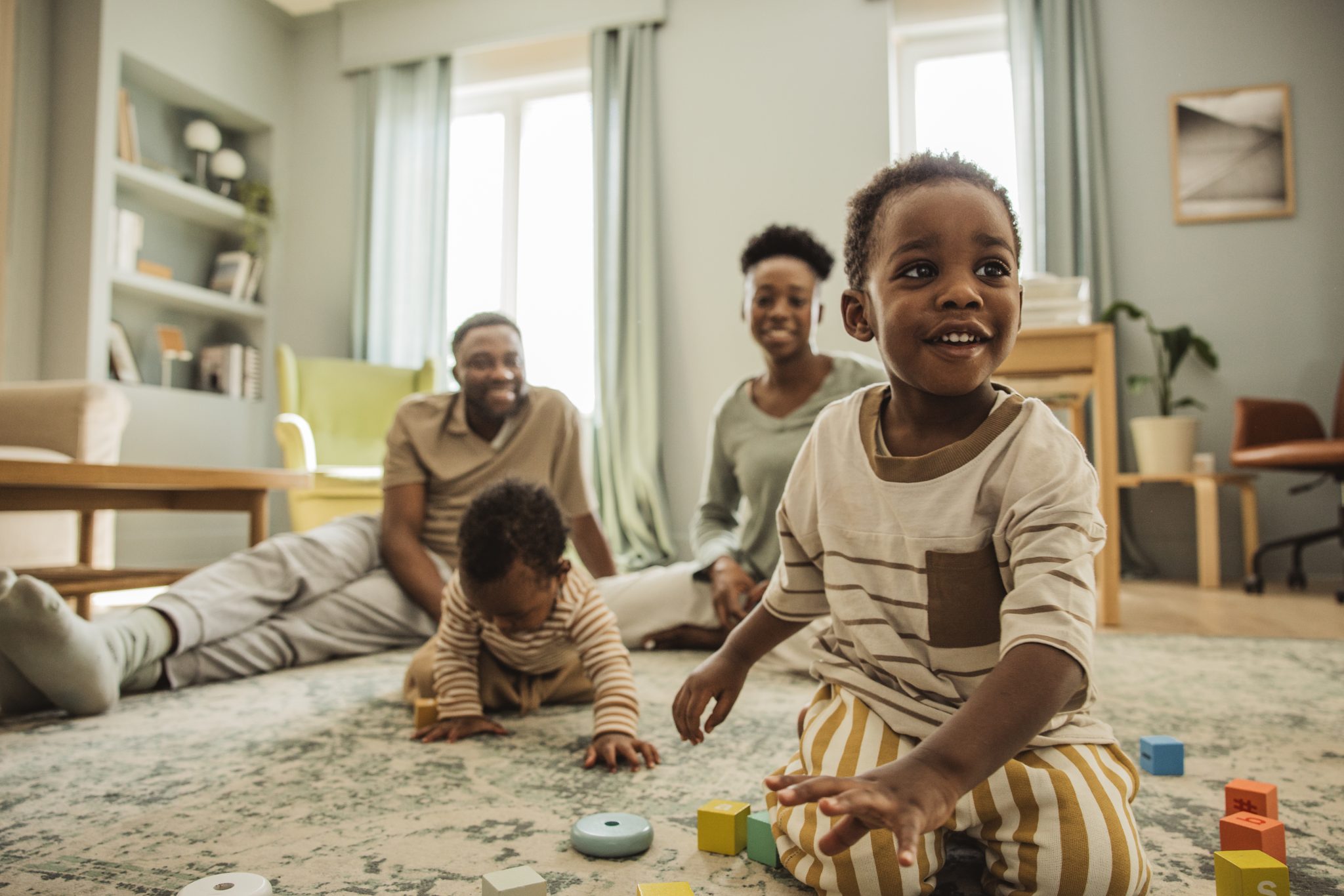 A family at home, a young child playing with wooden blocks on the floor