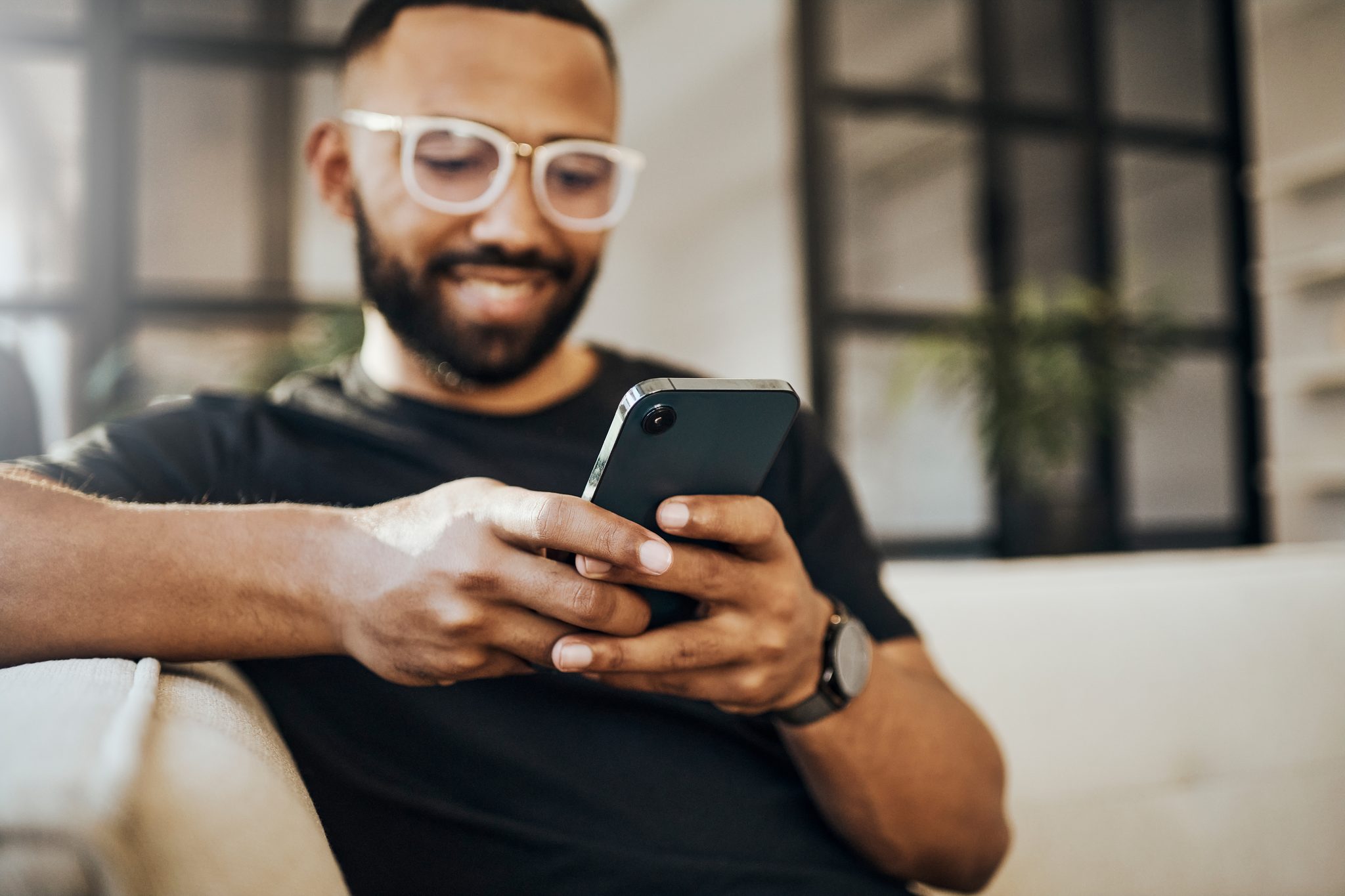 A man sitting on a sofa, smiling at his phone