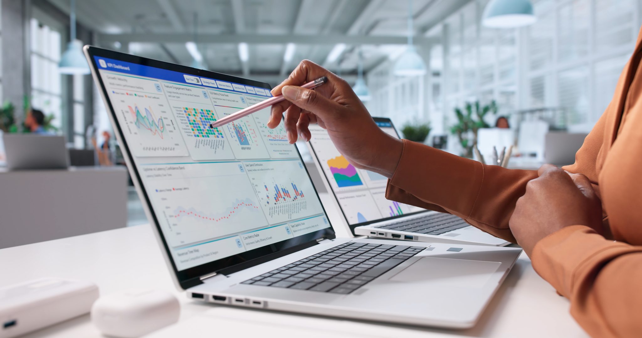 An analyst pointing a stylus at a laptop dashboard of healthcare charts and performance metrics